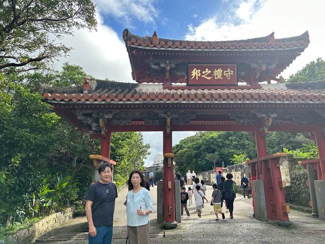 守礼門の前で、沖縄観光タクシーのドライバーと一緒に記念撮影するご夫婦